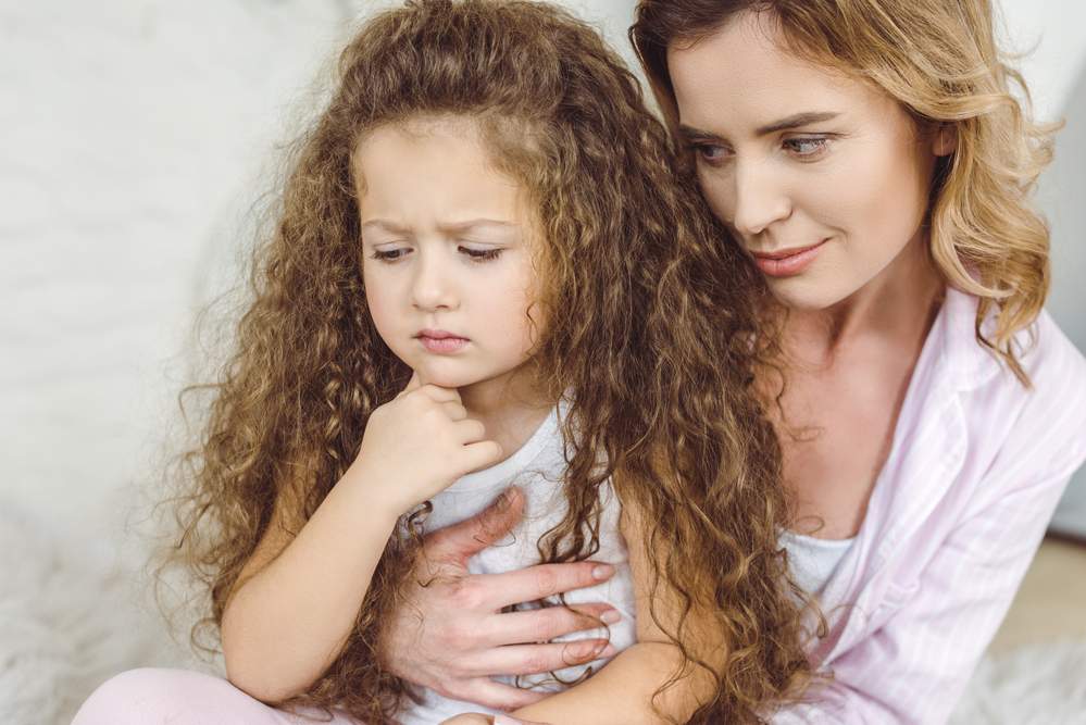 Sad little girl being held and consoled by her mom who is showing empathy