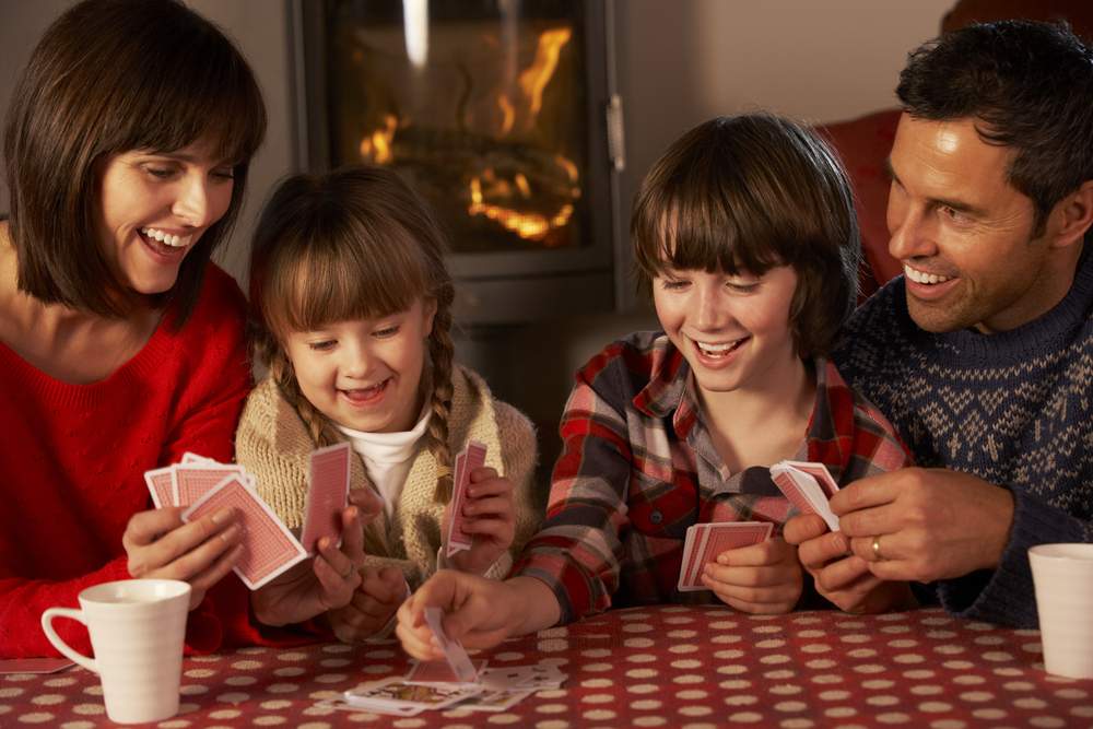 Portrait Of Family of four Playing Cards By Cozy Log Fire