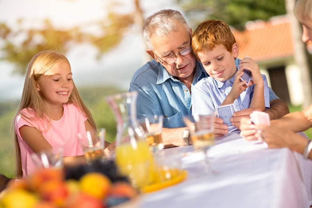 grandchildren playing cards with their grandfather outdoors around a table