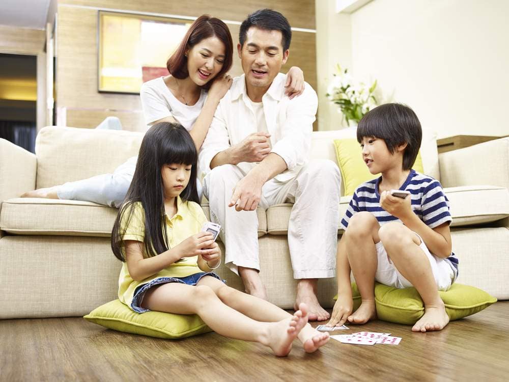 two asian parents watching children playing cards on floor.