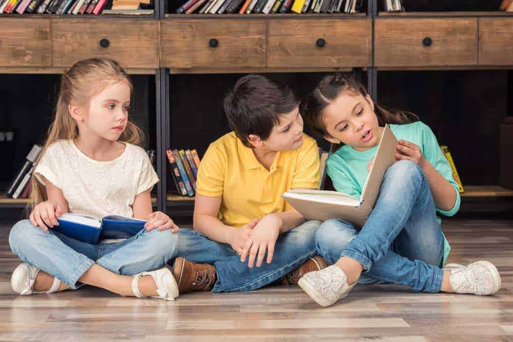three children sitting on the floor and reading books together
