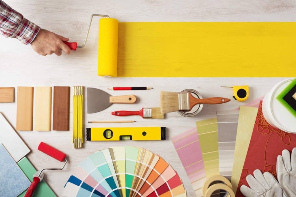 Decorator holding a painting roller and painting a wooden surface, work tools and swatches at bottom, banner with copy space. Clean Home Renovation Shows