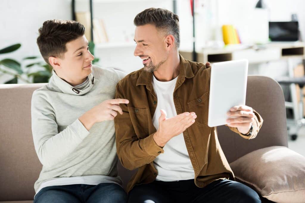 Father and son smiling and pointing at a tablet.