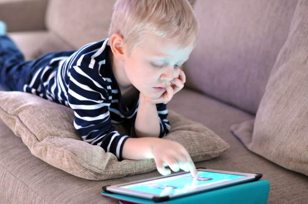 child laying on sofa playing with a tablet