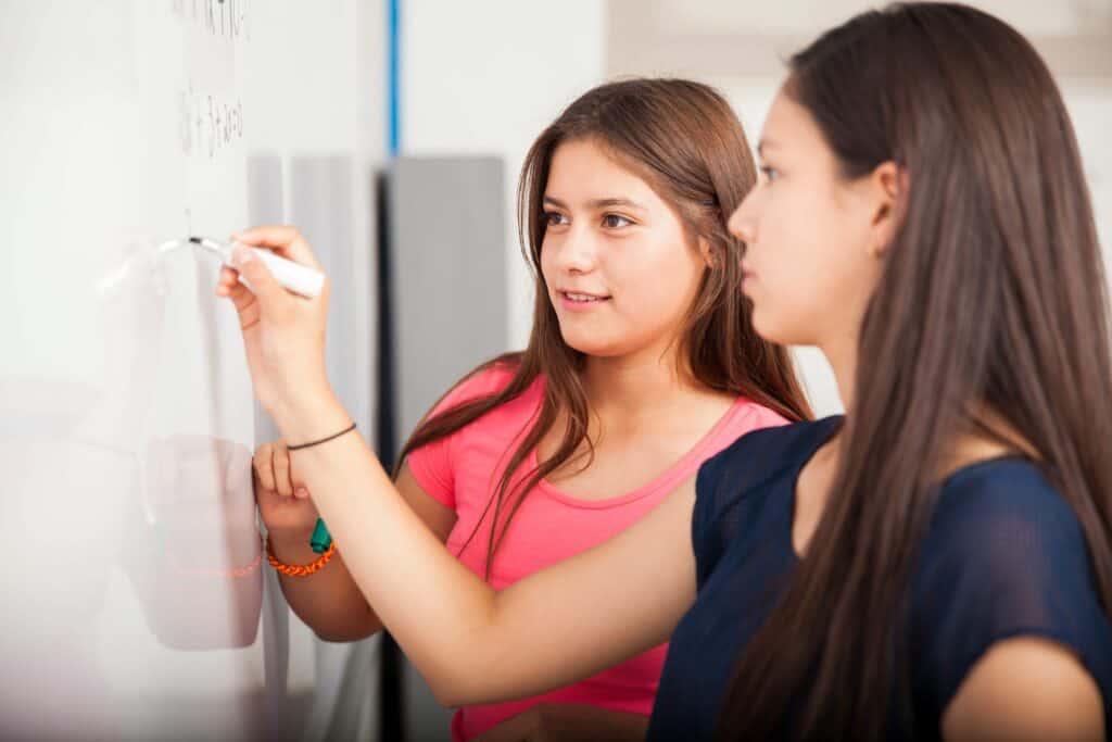 Couple of female high school students writing on a white board during class